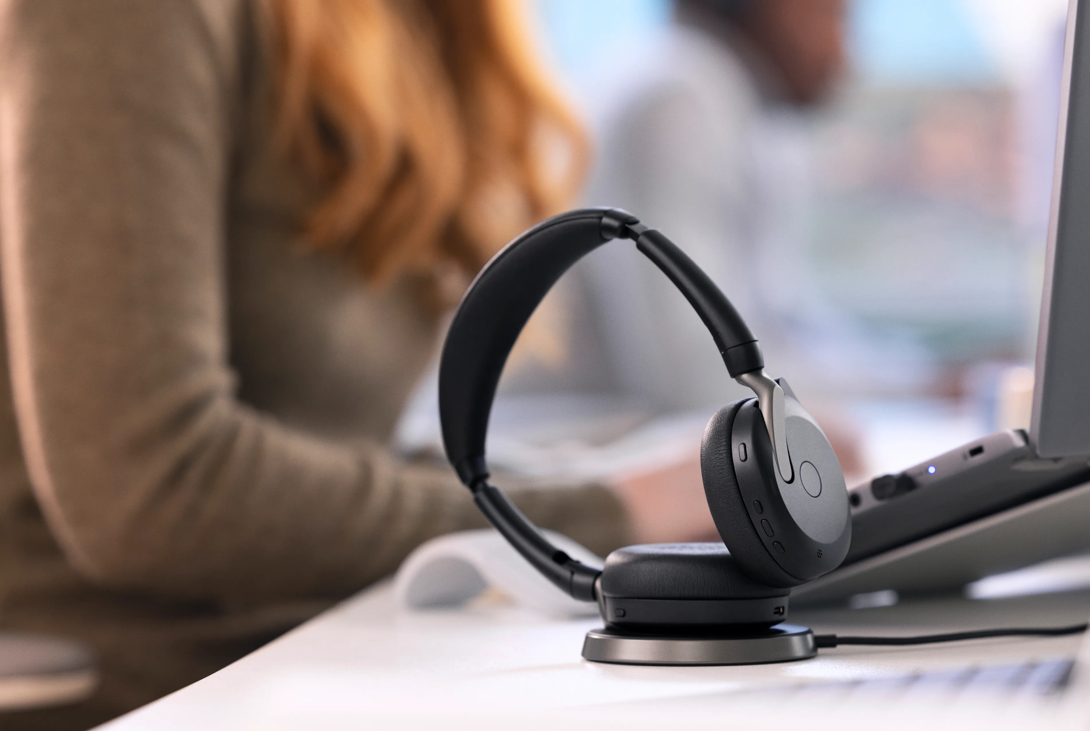 A woman at her desk, with Jabra Evolve2 65 Flex headphones connected to laptop